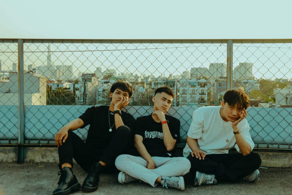 Three young men sitting on a rooftop, showcasing casual fashion and relaxed expressions.
